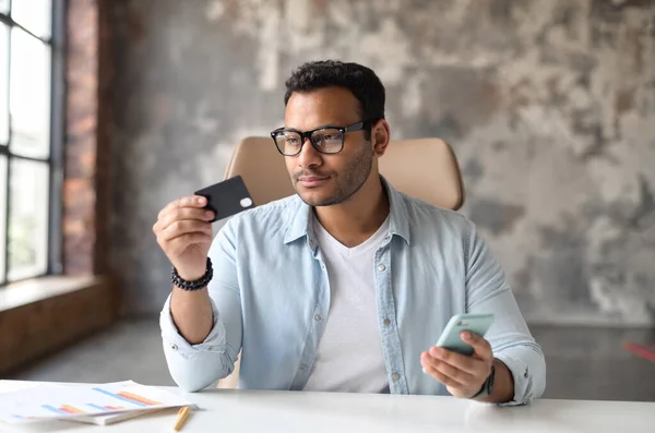 Serieuze indiaanse man met een creditcard en smartphone geld online overmaken — Stockfoto