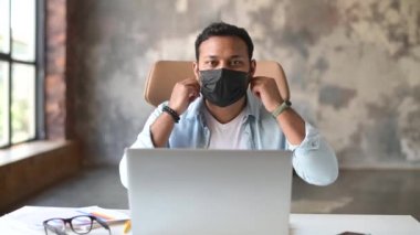 Neşeli Hintli erkek ofis çalışanı tıbbi koruyucu maskeyi çıkarıyor.