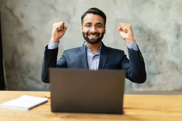 Excited and happy Indian businessman celebrating good deal or win sitting at desk