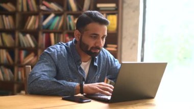 Hüsrana uğramış Hintli serbest çalışan adam üzgün bir ifadeyle dizüstü bilgisayara bakıyor.