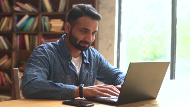 Positivo indio freelancer masculino mira el monitor del ordenador portátil — Vídeo de stock