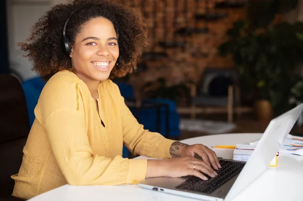 Mujer afroamericana joven que usa auriculares con computadora portátil para trabajo remoto —  Fotos de Stock