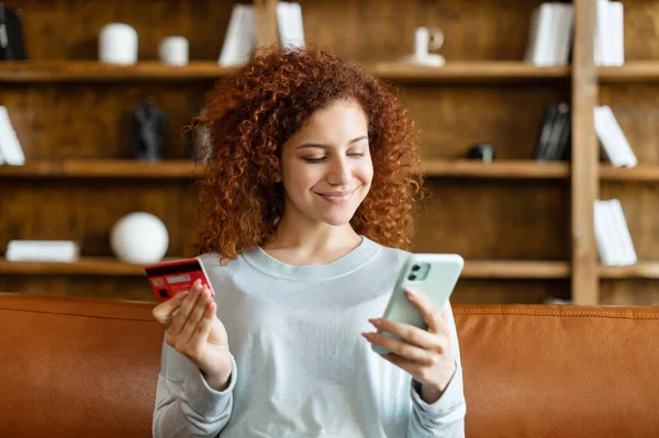 Tevreden glimlachende jonge vrouw met krullend kapsel zitten op de bank — Stockfoto