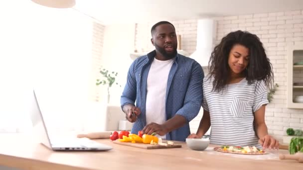 Glückliches multiethnisches Paar bereitet gemeinsam vor einem Laptop das Essen zu — Stockvideo