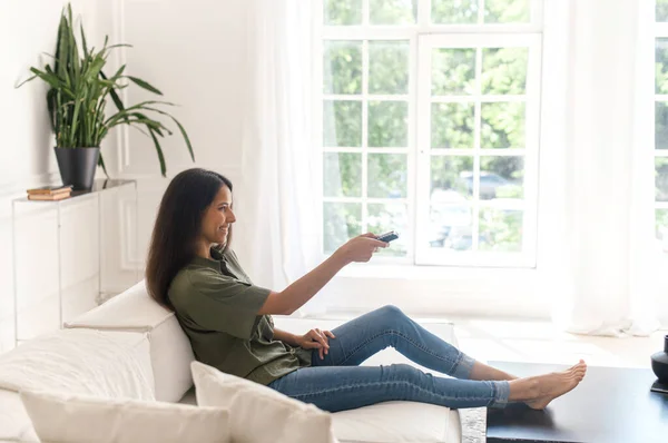 Indian woman lying on the comfortable white sofa with remote controller