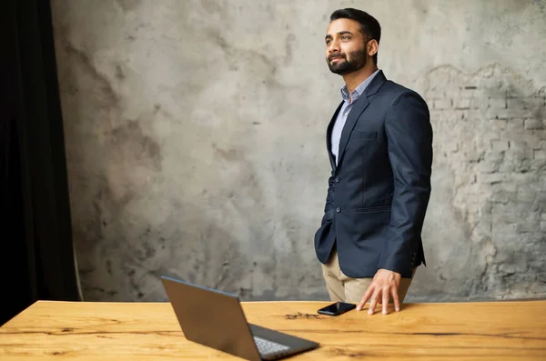 Indian businessman in formal suit leaned on the desk and looks away — Stock Photo, Image