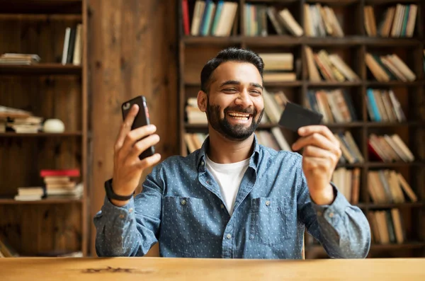 Hombre barbudo indio con camisa casual inteligente con tarjeta bancaria de crédito y teléfono inteligente —  Fotos de Stock