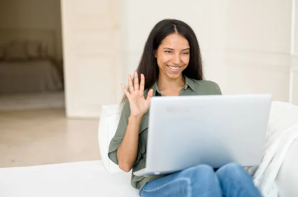 Young cheerful multiethnic woman waving hello to online interlocutor, using laptop — Stock Photo, Image