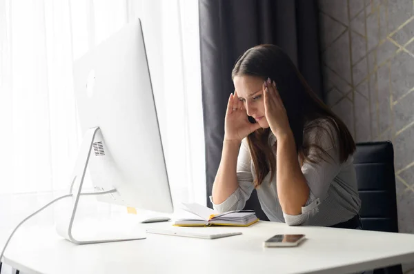 Mujer joven perturbada concentrada sentada en el escritorio frente a la PC —  Fotos de Stock