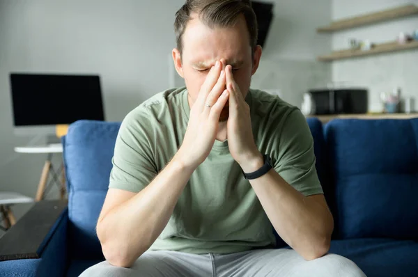 Upset young man sitting on the couch at home with hands on face — Stock Photo, Image