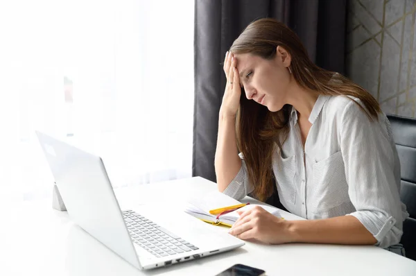 Mujer freelancer cansado siente estrés, sostiene la frente y mira la pantalla del ordenador portátil —  Fotos de Stock