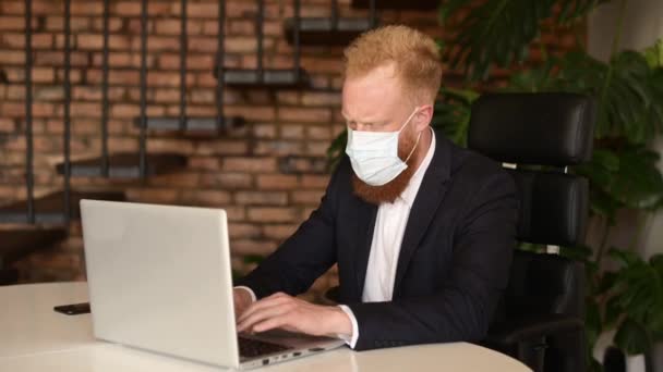 Allvarlig rödhårig affärsman i smart casual kostym bär skyddande ansiktsmask — Stockvideo