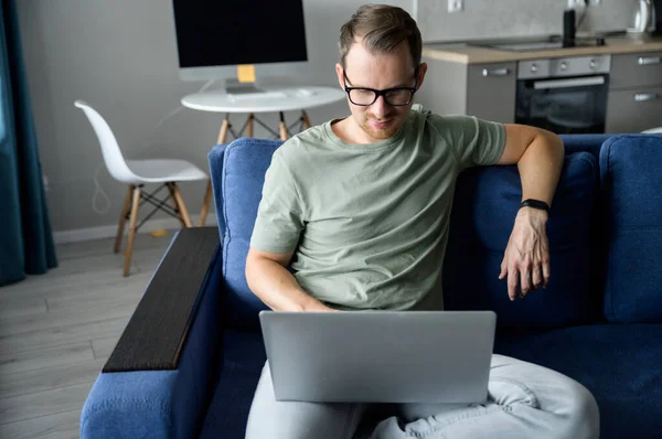 Привлекательный улыбающийся мужчина сидит на диване в гостиной, используя ноутбук — стоковое фото