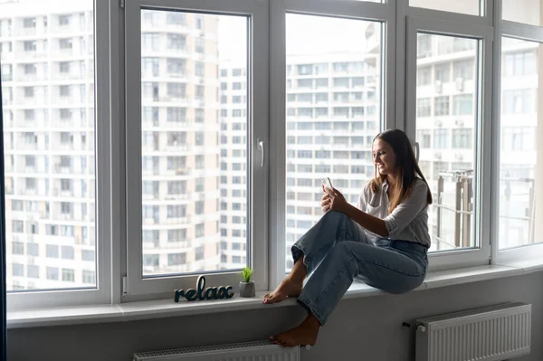 Mulher feliz e sorridente em camisa casual usando smartphone no apartamento moderno — Fotografia de Stock