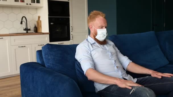 Pensiv rödhårig man bär skyddande medicinsk mask ser åt sidan med rädsla i ögonen — Stockvideo