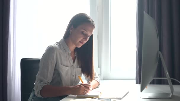 Концентрированная молодая женщина учится онлайн, смотрит вебинар и делает заметки — стоковое видео