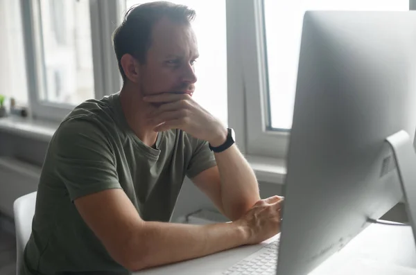 Konzentrierter junger Mann im T-Shirt, der mit einem trendigen PC aus der Ferne arbeitet — Stockfoto