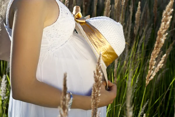 Pregnant  womans belly with the hat in sunbeams — Stock Photo, Image