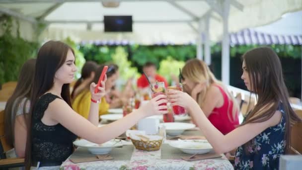 Obiad w restauracji, urocze dziewczyny cieszyć relaks w restauracji lub kawiarni, jedzenie i picie koktajli i za pomocą ich smartfona — Wideo stockowe