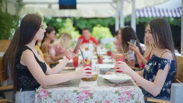 Lunch met vrienden, vrolijke mooie meisjes genieten van ontspannen in cafe of restaurant en communiceren met vriendinnen online met behulp van hun smartphone — Stockvideo