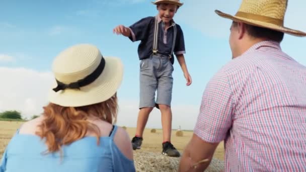 Életmód, kisfiú szórakozás játszani szénakazalban a szülők gördülő bála mező — Stock videók