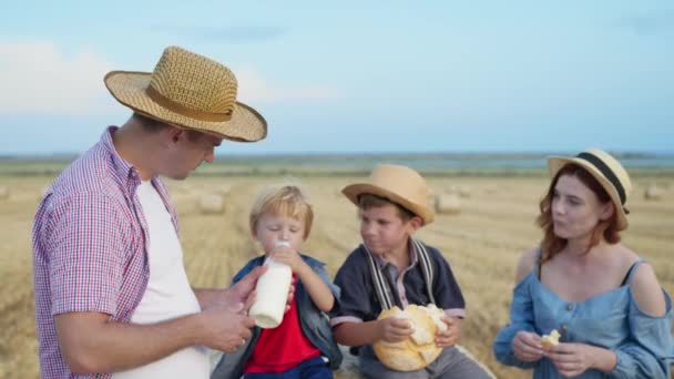 Család a pikniken, apa a feleségével és fiai kenyeret esznek és tejet mosnak a búzamezőn — Stock videók