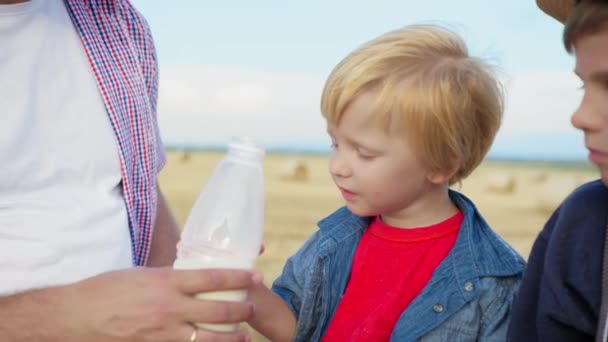 Niño en el picnic, niño come pan y bebe leche de la botella con la ayuda de papá durante las vacaciones familiares en el campo — Vídeos de Stock