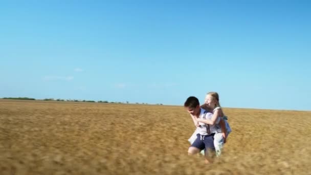 Amigos se divertir juntos ao ar livre, menino carrega uma menina em suas costas e corre alegremente no campo de trigo no fundo do céu azul — Vídeo de Stock