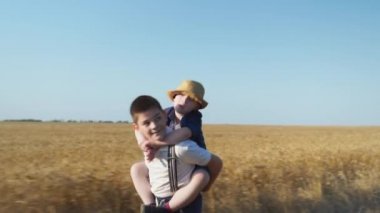 Çocuklar buğday tarlasında birlikte eğleniyor. Oğlan sırtında Down sendromlu bir arkadaşını taşıyor.