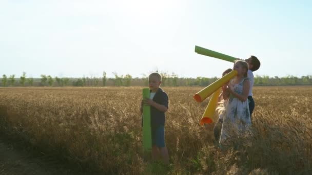 Děti v přírodě, šťastní přátelé flákat se s velkými trubkami v rukou v pšeničném poli ve večerních hodinách venku — Stock video