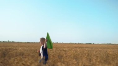 Açık hava oyunları, yüzünde duygular olan çocuk mavi gökyüzünün arka planındaki buğday tarlasında kağıt uçakla oynuyor.