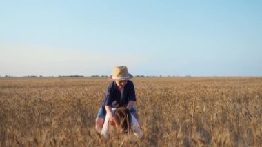 Çocuk arkadaşını sırtında sendromla kaldırıyor ve kameraya poz veriyor. Mavi gökyüzünün arkasındaki buğday tarlasında gülümseyen kırsal çocuklar.
