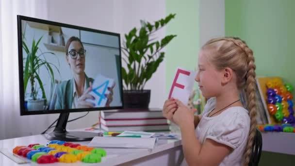 Fjärr utbildning under pandemi, trevlig liten flicka visa kort till lärare på skolan online kurs medan du sitter hemma med en dator — Stockvideo