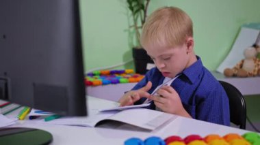 Çevrimiçi öğrenme, Down sendromlu okul çocuğu Coronavirus zamanlarında bilgisayarın başında oturan matematik eğitimi sırasında sayılarla kartları gösteriyor.