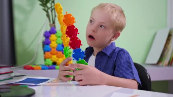 Criança com deficiência está brincando com brinquedos coloridos enquanto se senta à mesa em casa, menino com síndrome de Down está estudando um novo construtor — Vídeo de Stock