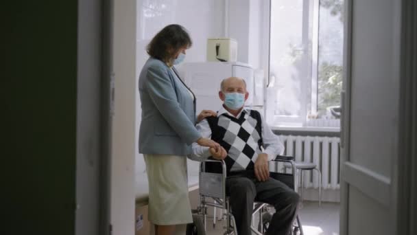 Älteres Ehepaar in Schutzmasken stützt sich bei Krankheit gegenseitig, Rentner im Rollstuhl im Gespräch mit älterer Frau im Krankenhaus — Stockvideo