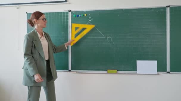 Aula de matemática on-line na escola, ensino de pedagogia para seus alunos via chamada de vídeo em pé no quadro-negro olha para a câmera e fala em sala de aula — Vídeo de Stock