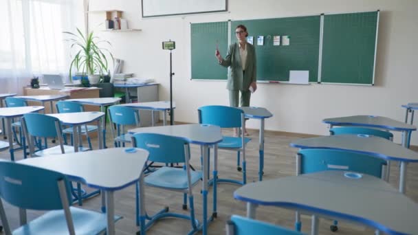 Pedagogo em sala de aula vazia com régua na mão perto de quadro-negro usando câmera de vídeo celular gravando-se durante o ensino de matemática on-line na escola — Vídeo de Stock