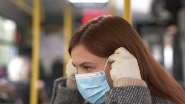 Kadın otobüse biniyor ve virüs ve enfeksiyondan korunmak için tıbbi maske takıyor. Kadın yolcu öksürüyor ve toplu taşıma araçlarında tırabzanlara tutunuyor.