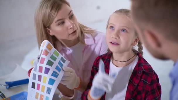 Οικογενειακό χρόνο μαζί με την κόρη κατά τη διάρκεια της ανακαίνισης του διαμερίσματος, ζευγάρι και παιδί κορίτσι με παλέτα επιλέξτε χρώματα για τη ζωγραφική του τοίχου στο σπίτι — Αρχείο Βίντεο