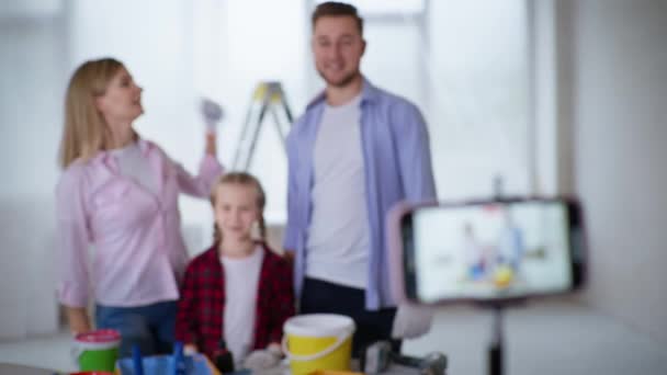 Telefoon neemt video tijdens de reparatie, vrolijk jong stel bloggers en chid meisje met palet kiezen kleuren voor het schilderen van de muur in het appartement — Stockvideo