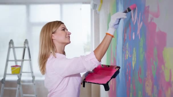 Ανακαίνιση και σύγχρονη τέχνη, κορίτσι κρατήσει δίσκο με ροζ χρώμα και πινέλο κατά τη διάρκεια της διαδικασίας ζωγραφικής σε ένα λευκό τοίχο στο σπίτι — Αρχείο Βίντεο