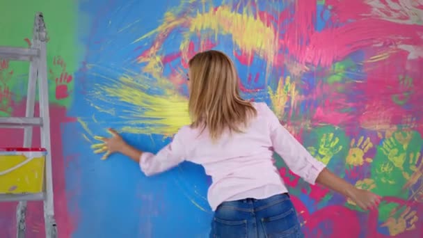 Активная художница с помощью пальцев она создает красочные, эмоциональные и чувственные картины, девушка рисует руками на стене, вид сзади — стоковое видео