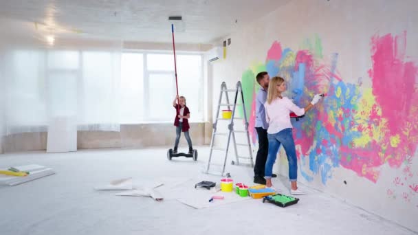 Modern gyermek festi a mennyezetet egy görgővel egy légdeszkán az új otthonban, a kislány segít a szülőknek a felújítás során — Stock videók