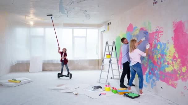 Enfant moderne peint le plafond avec rouleau sur un hoverboard dans un nouvel appartement, petite fille aide les parents pendant la rénovation — Video