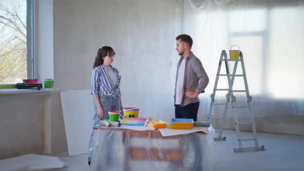 Pár hádky, otrávená dívka s paletou barev v rukou křičí na mladého muže během renovace v novém domově — Stock video