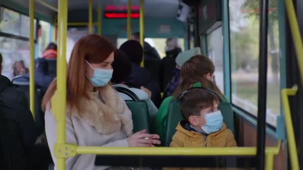 Passageira do sexo feminino com seu filho vestindo máscaras médicas trata as mãos com um anti-séptico para proteger contra vírus e infecção enquanto viaja no ônibus da cidade — Vídeo de Stock