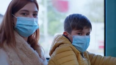 mother with male child wearing medical masks to protect against coronavirus while traveling on public bus, social distance