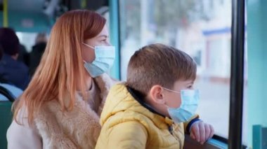 mother and male child take precautions and wear medical mask to protect against virus and infection while traveling on city bus