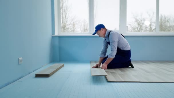 Travaux de finition, l'homme professionnel installe un panneau stratifié avec serrure sur des panneaux de mousse de polystyrène dans le nouvel appartement près de la fenêtre pendant la rénovation — Video